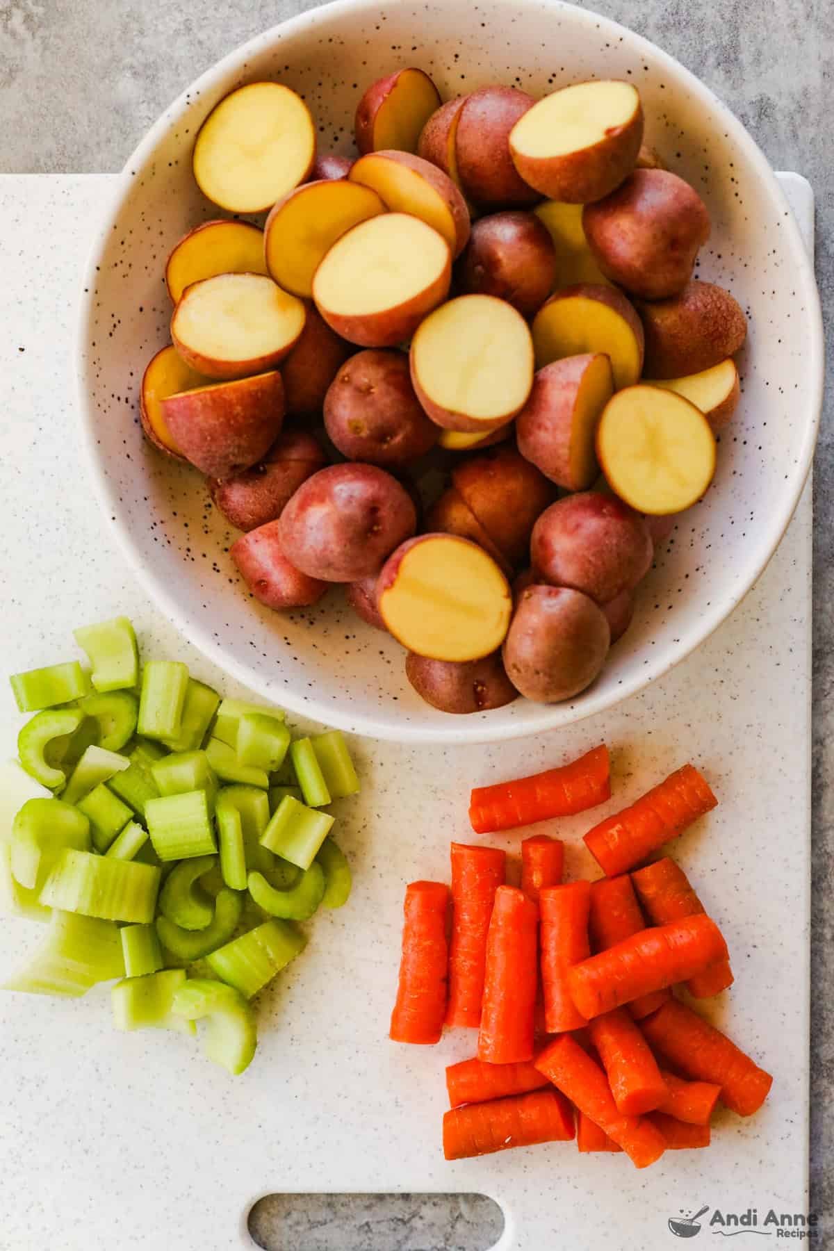 Halved baby potatoes in a bowl, chopped celery, and roughly chop carrots on a cutting board.
