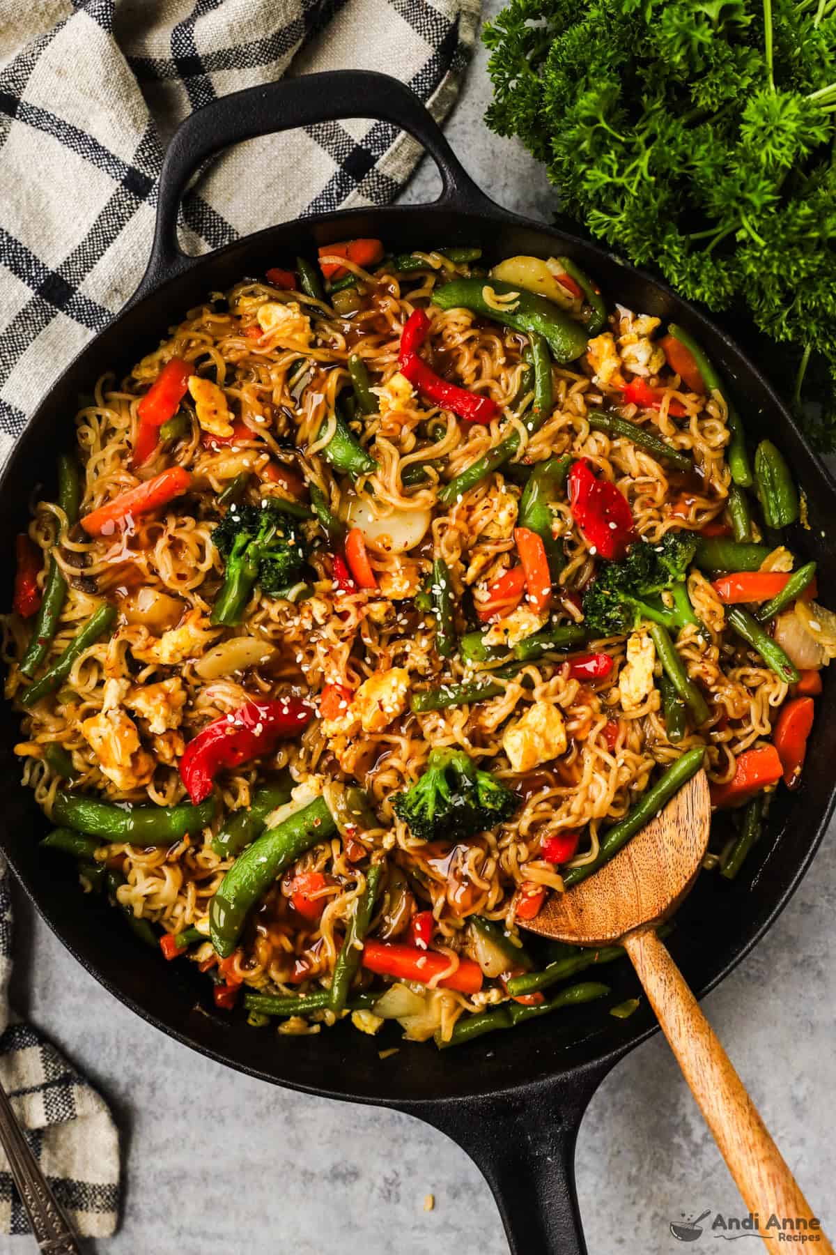 A skillet with ramen noodles, snap peas, bell peppers, carrots, and green beans in a teriyaki sauce topped with sesame seeds.