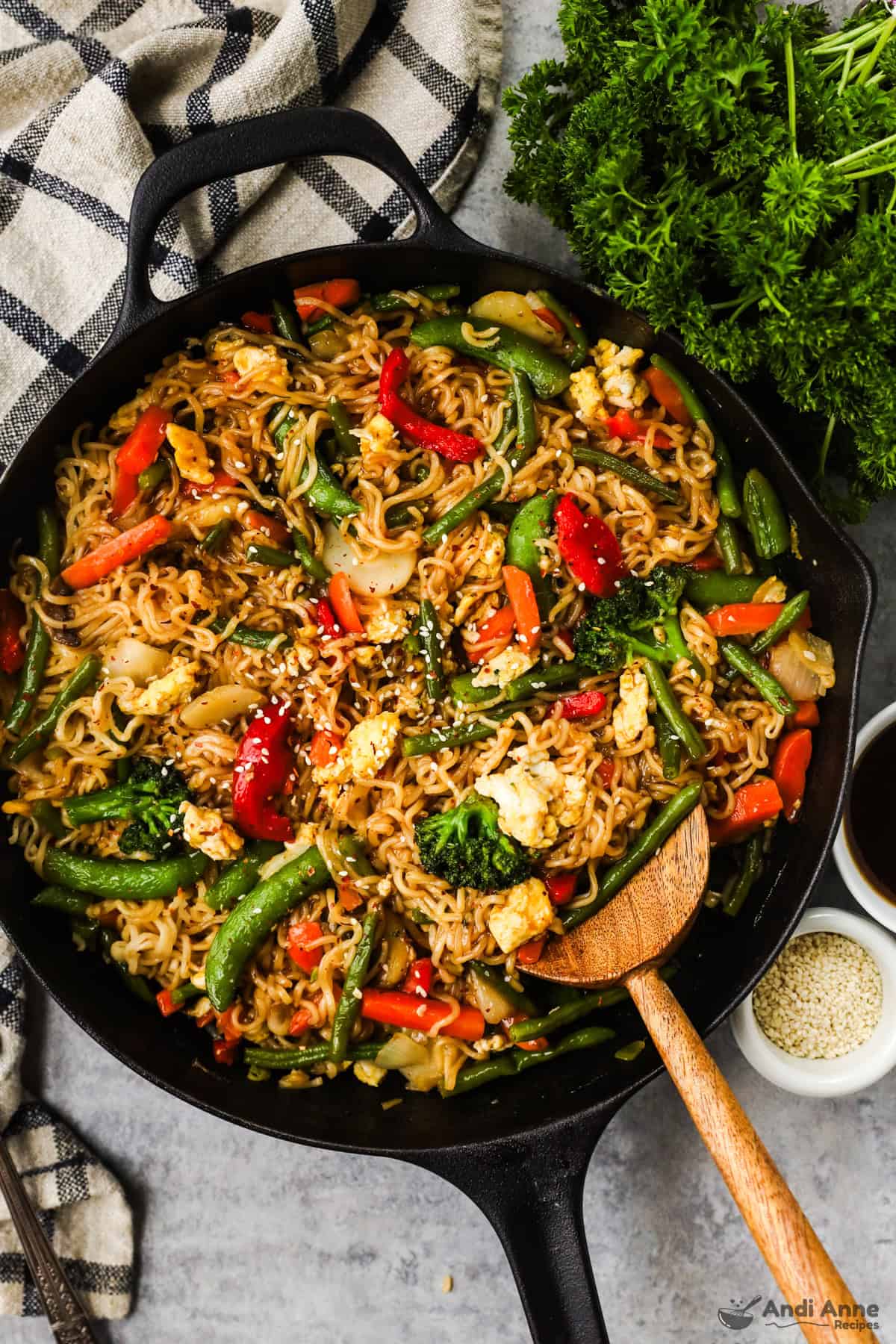 A skillet with ramen noodles, snap peas, bell peppers, carrots, and green beans in a teriyaki sauce topped with sesame seeds.