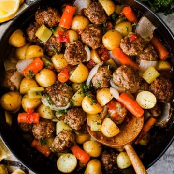 A casserole dish with homemade meatballs, halved baby potatoes, and carrots baked in tomato gravy, ready to serve.