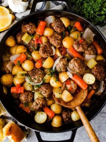 A casserole dish with homemade meatballs, halved baby potatoes, and carrots baked in tomato gravy, ready to serve.