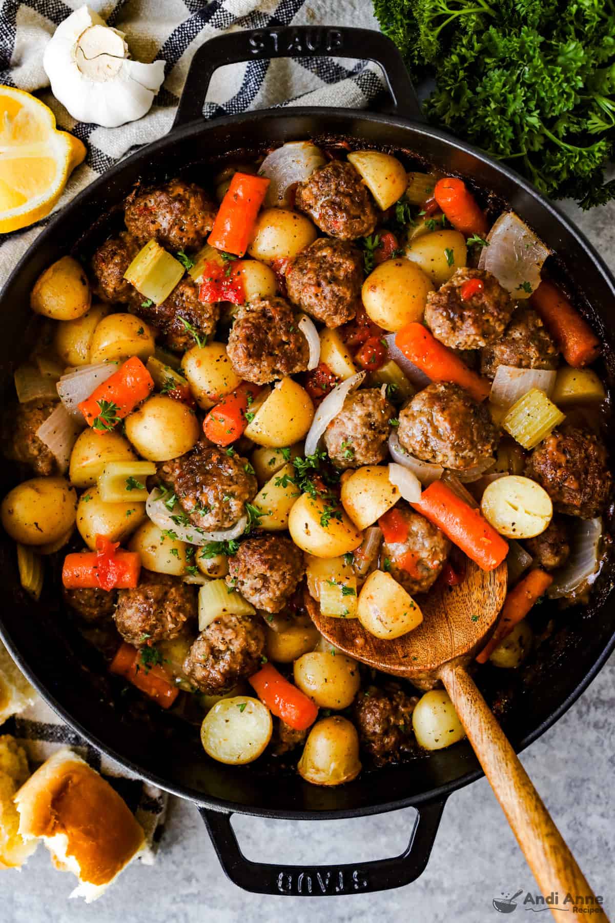 A casserole dish with homemade meatballs, halved baby potatoes, and carrots baked in tomato gravy, ready to serve.
