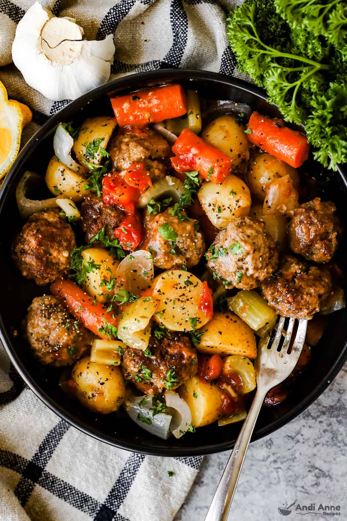 A skillet filled with meatballs, potatoes, onions, and carrots in thick tomato gravy.