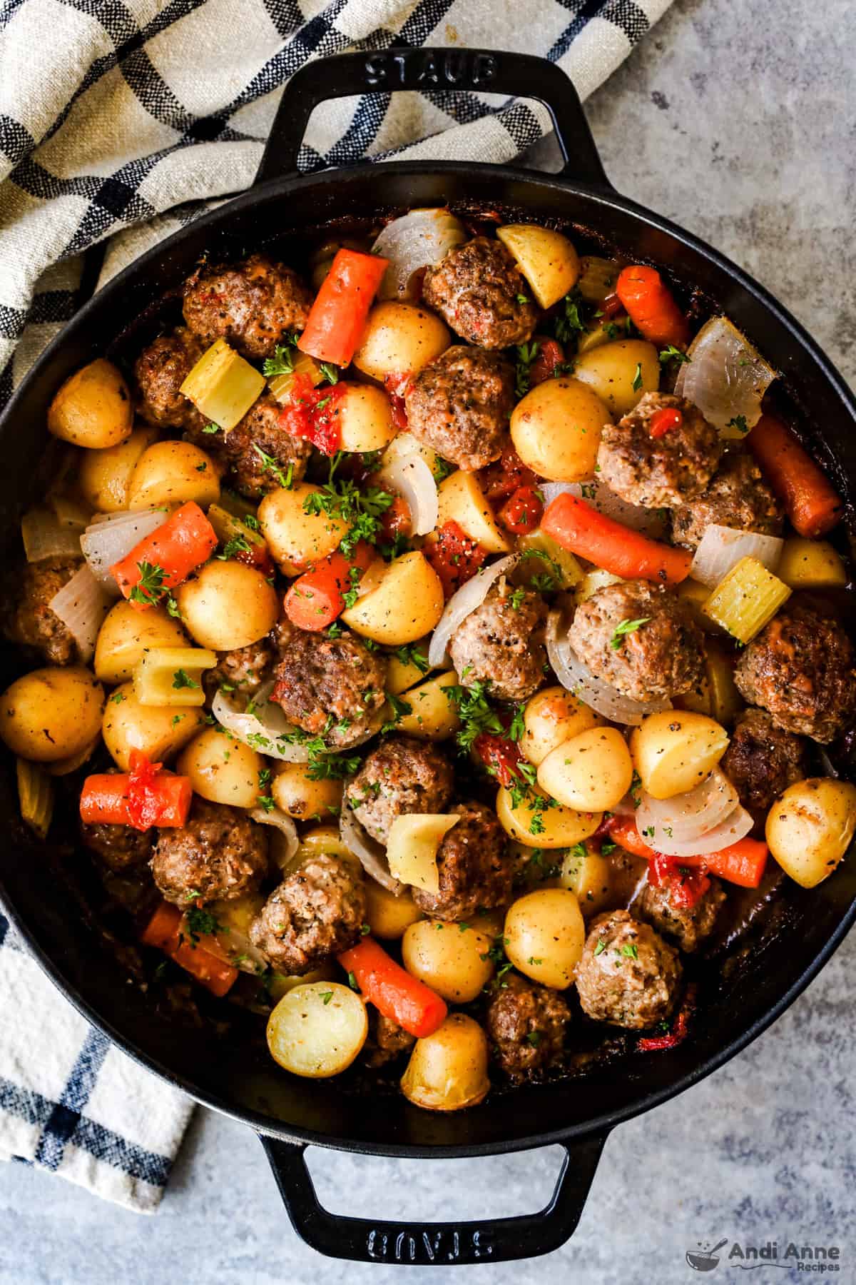 A skillet filled with meatballs, potatoes, onions, and carrots in thick tomato gravy.