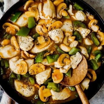 A large skillet with mushrooms, chicken, and green bell peppers in an onion soup gravy.