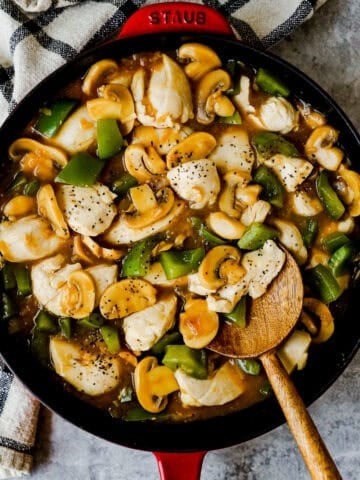 A large skillet with mushrooms, chicken, and green bell peppers in an onion soup gravy.