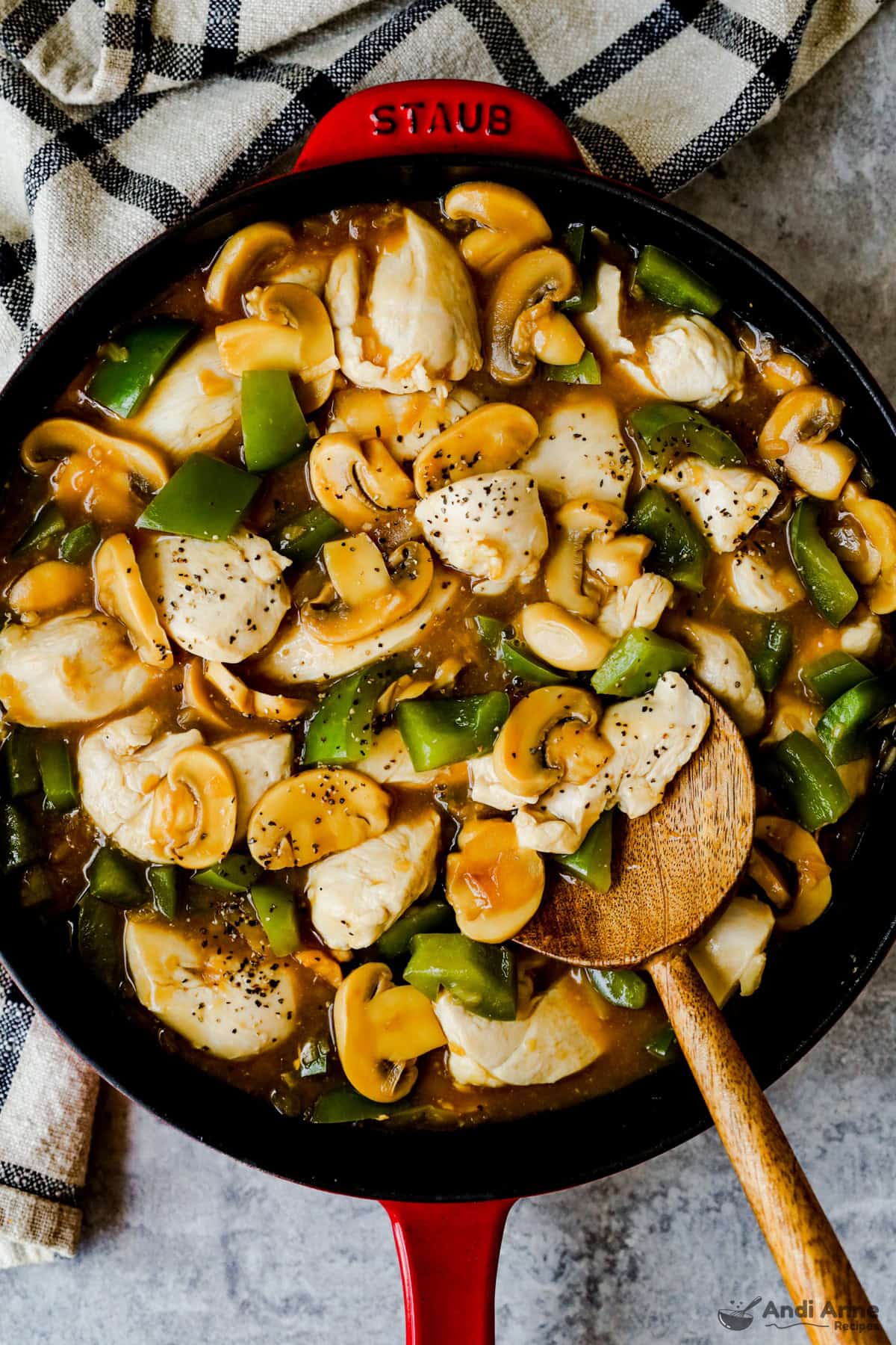 A large skillet with mushrooms, chicken, and green bell peppers in an onion soup gravy.