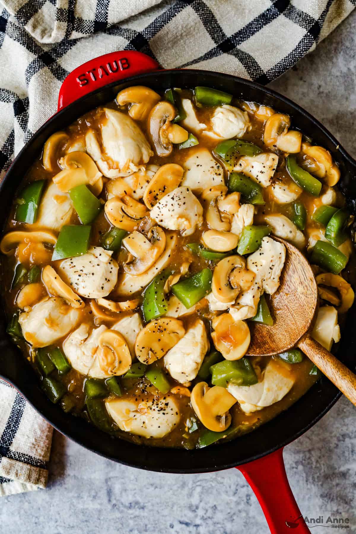 Chicken, mushrooms, and green bell peppers in an onion soup gravy in a large skillet with a wooden spoon.