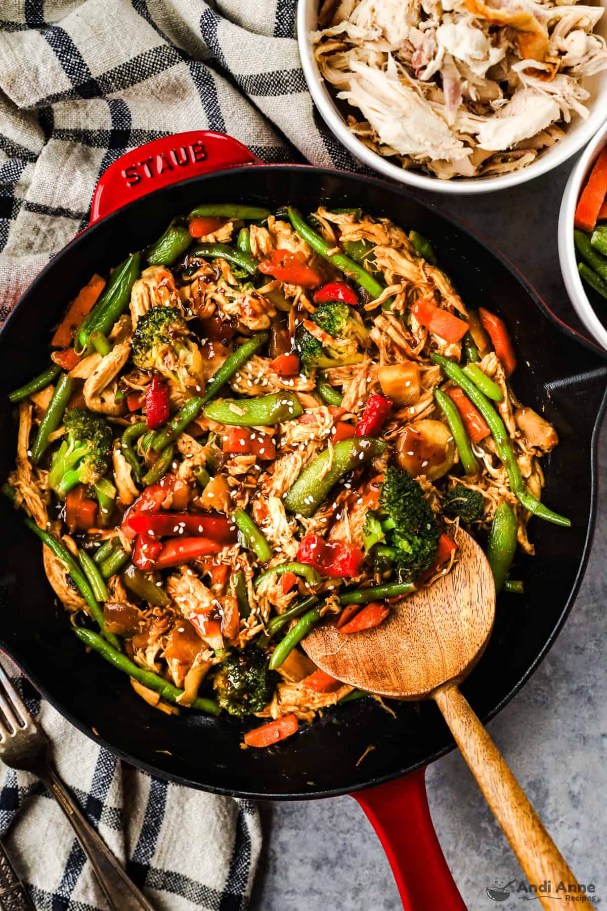A skillet with shredded rotisserie chicken, carrots, green beans, bell peppers, and snap peas in stir fry sauce, and topped with sesame seeds.