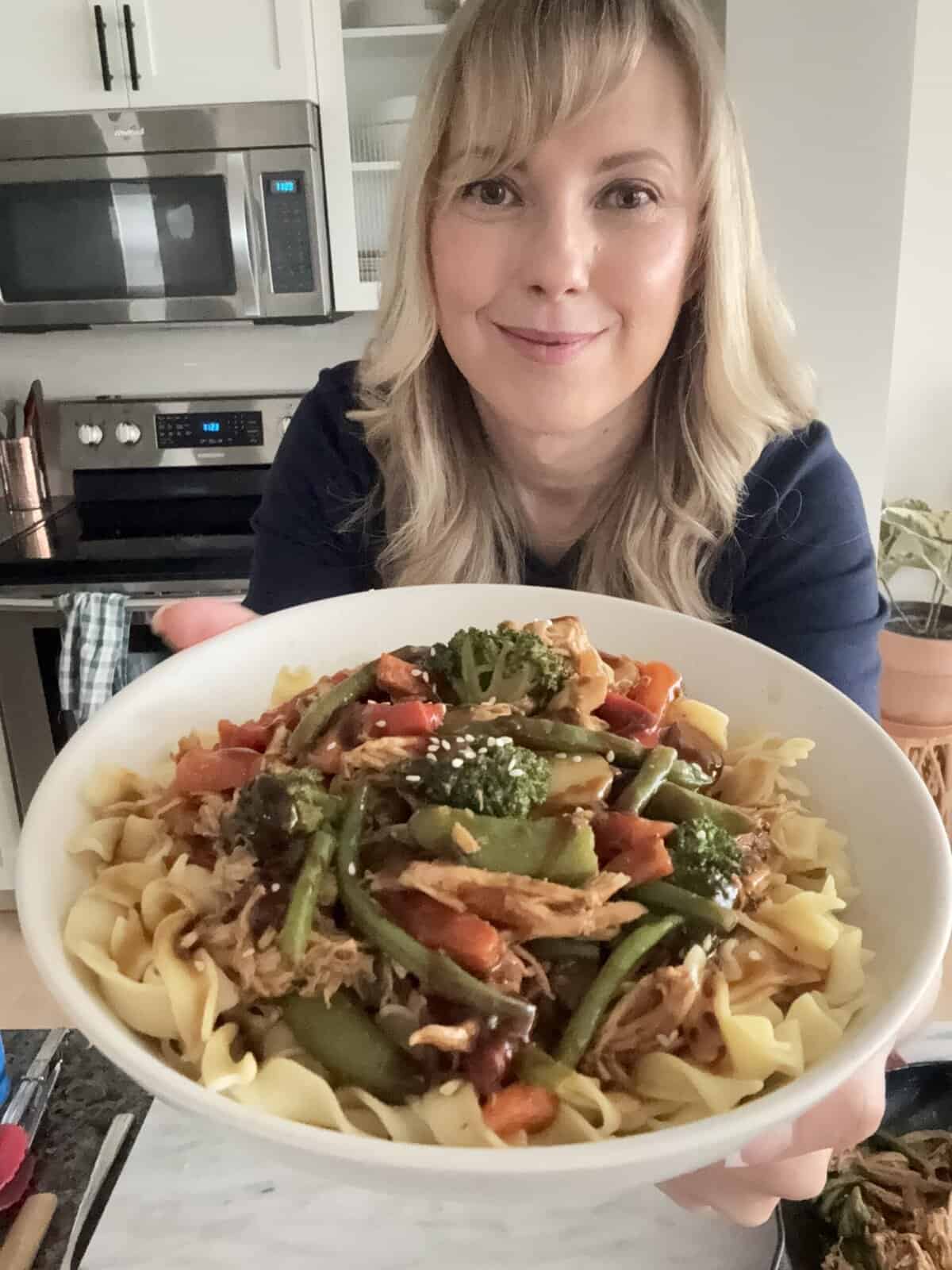 Shredded rotisserie chicken, carrots, green beans, bell peppers, and snap peas in stir fry sauce, topped with sesame seeds on a bed of egg noodles.