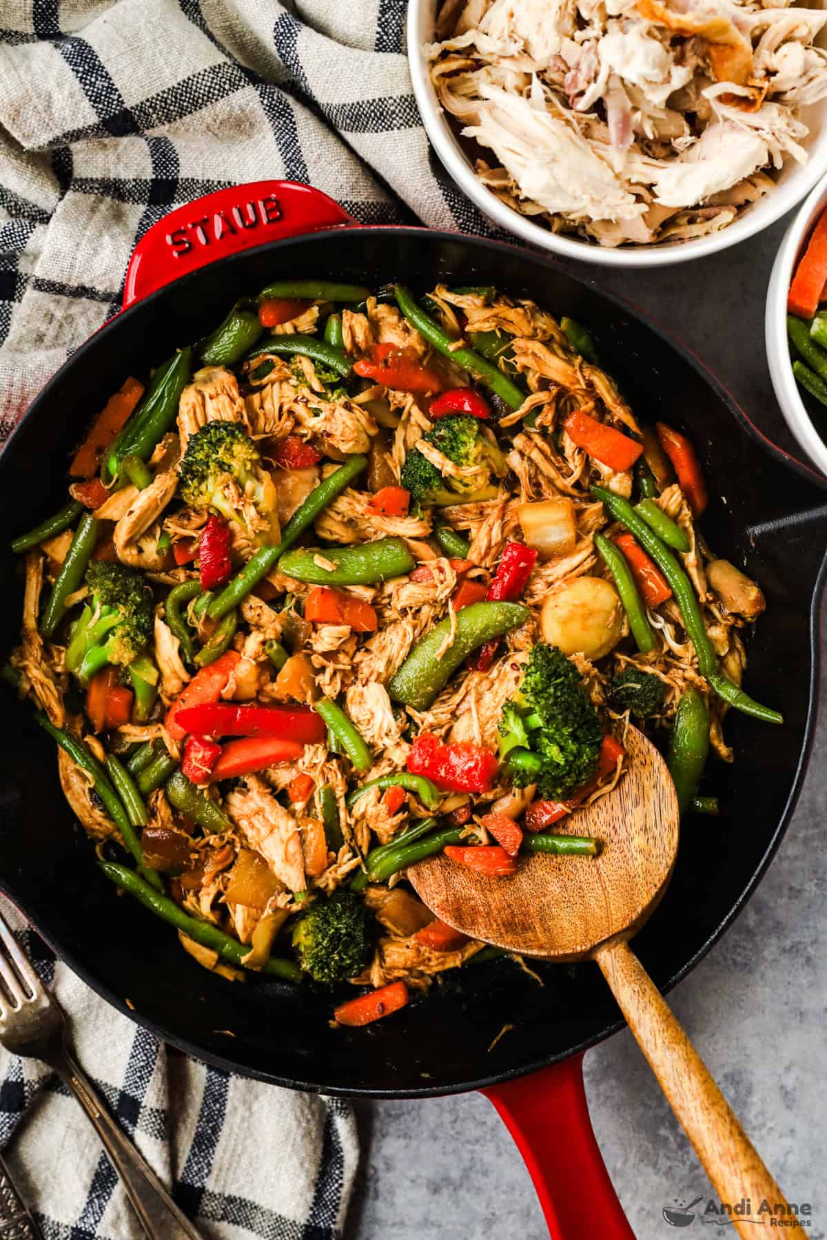 A skillet with shredded rotisserie chicken, carrots, green beans, bell peppers, and snap peas in stir fry sauce, and topped with sesame seeds.