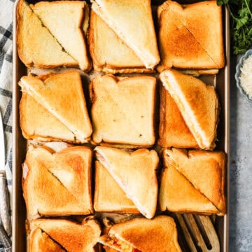 A sheet pan with 11 grilled cheese sandwiches that are cut in half diagonally.