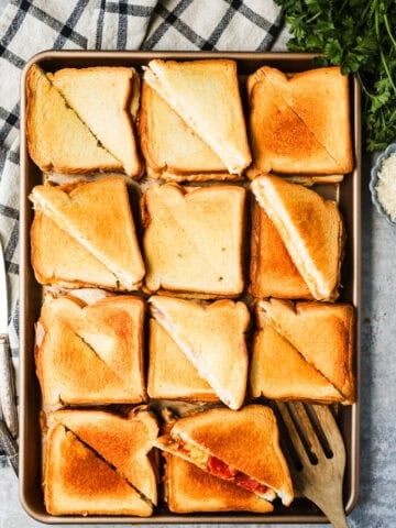 A sheet pan with 11 grilled cheese sandwiches that are cut in half diagonally.