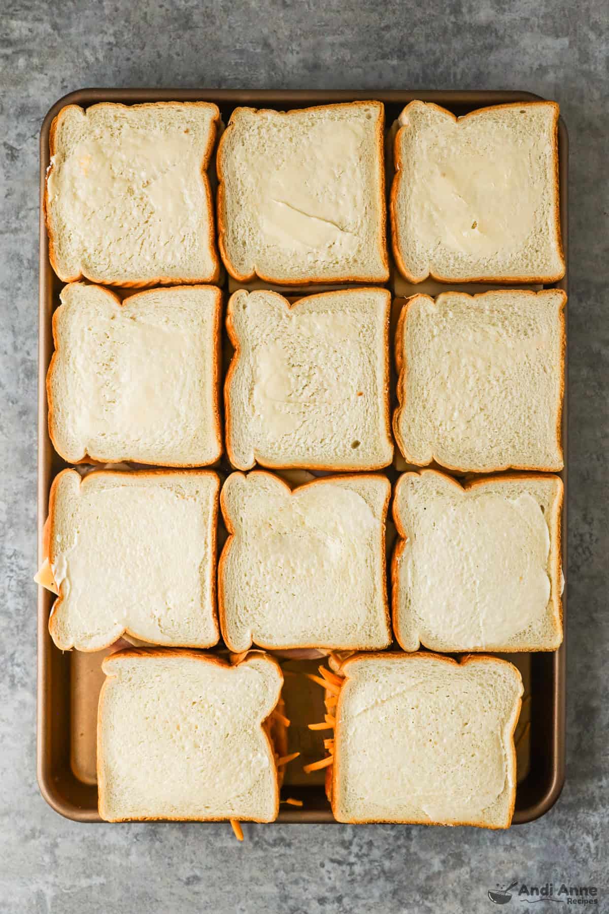 Cheese sandwiches with butter on the top slice on a sheet pan before baking.