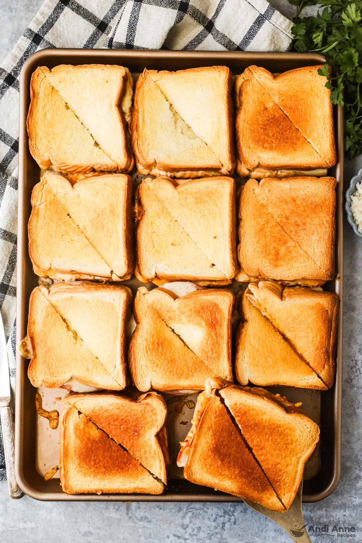 Eleven grilled cheese sandwiches sliced diagonally on a sheet pan.