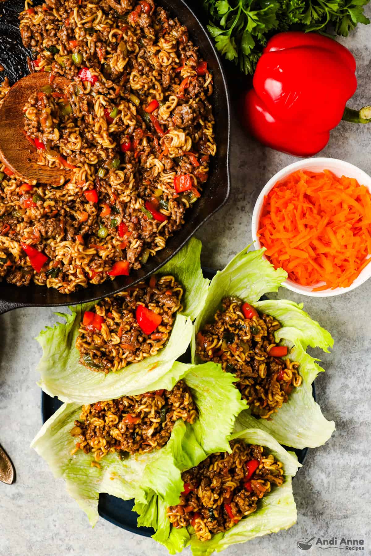 A skillet with ground beef, ramen noodles, and vegetables in a teriyaki sauce filling, and lettuce leaves filled with the filling.