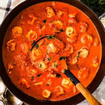 A large pot of creamy tomato soup with tortellini and Italian sausage topped with parsley.