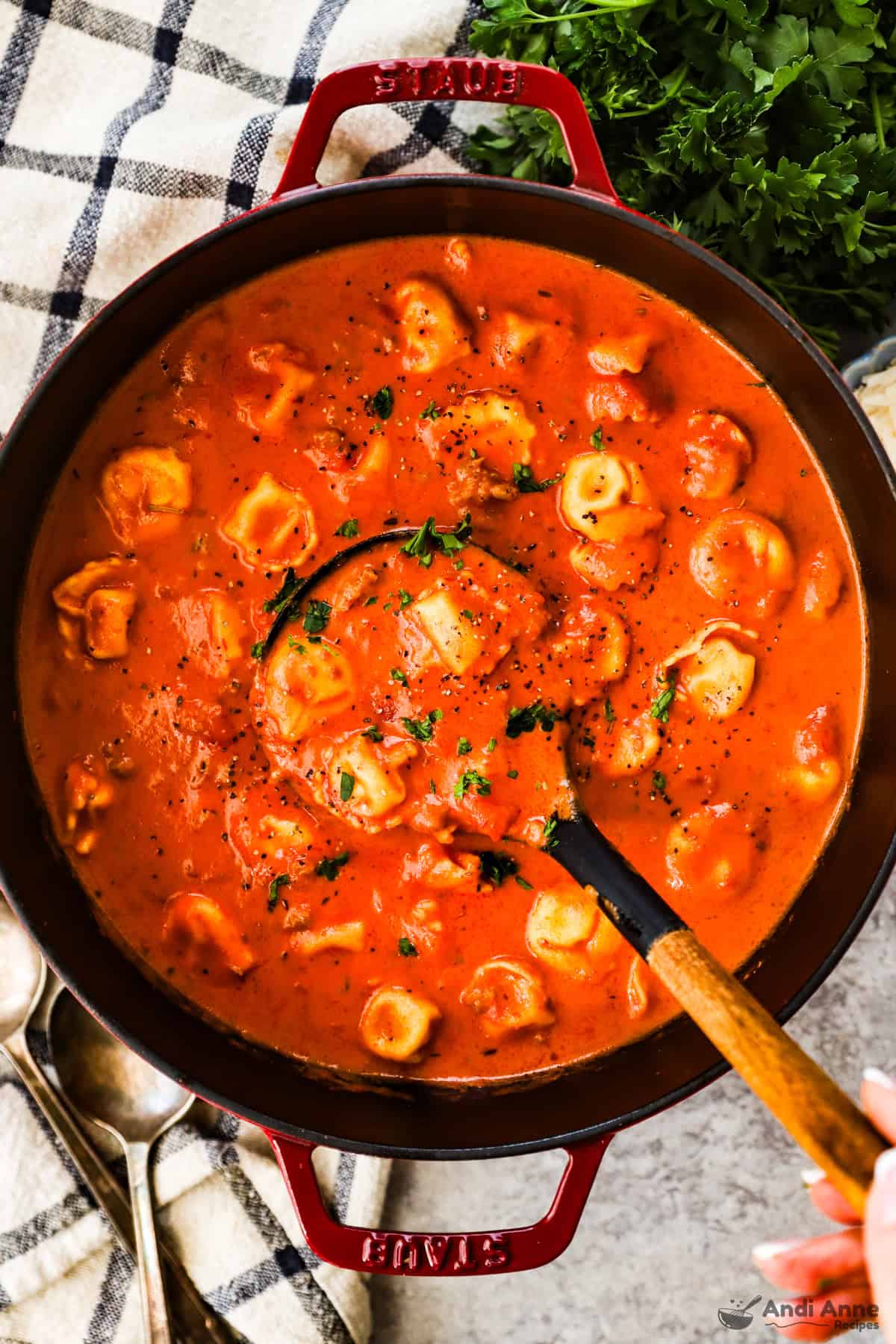 A large pot of creamy tomato soup with tortellini and Italian sausage topped with parsley.