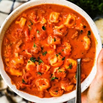A large bowl of creamy tomato soup with tortellini and Italian sausage topped with parsley.