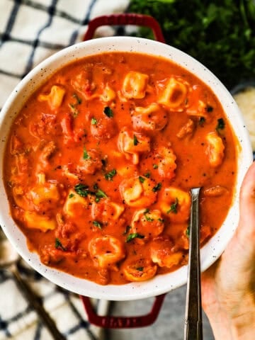A large bowl of creamy tomato soup with tortellini and Italian sausage topped with parsley.