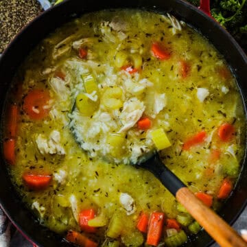 A large pot of chicken and rice soup with a ladle.