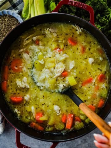 A large pot of chicken and rice soup with a ladle.