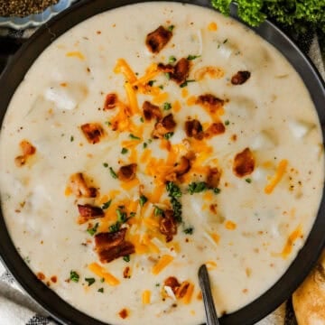A large bowl of baked potato soup loaded with bacon, cheddar cheese, and chives.