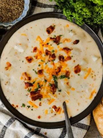 A large bowl of baked potato soup loaded with bacon, cheddar cheese, and chives.
