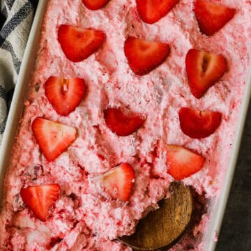 A large baking dish with strawberry angel food cake dessert, and a wooden spoon, removing a piece.