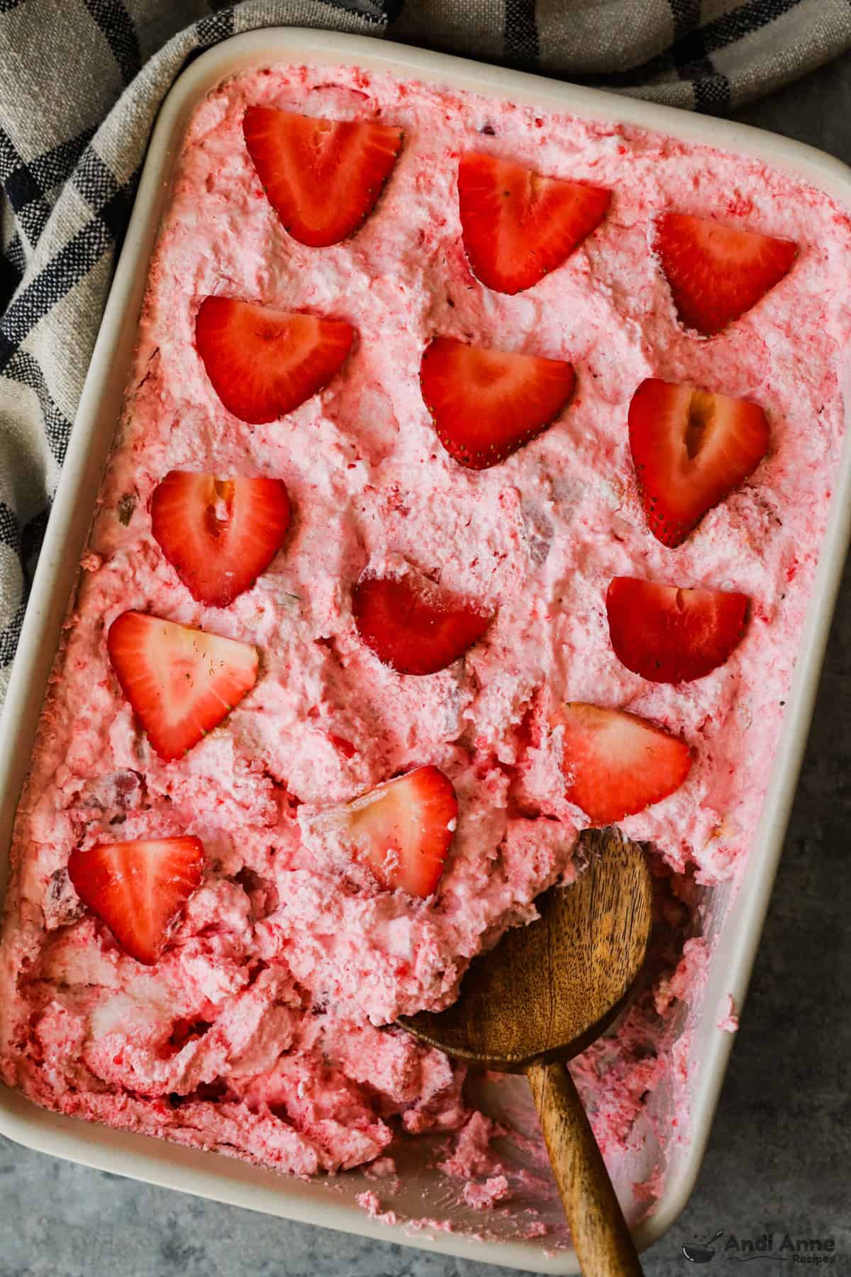 A large baking dish with strawberry angel food cake dessert, and a wooden spoon, removing a piece.