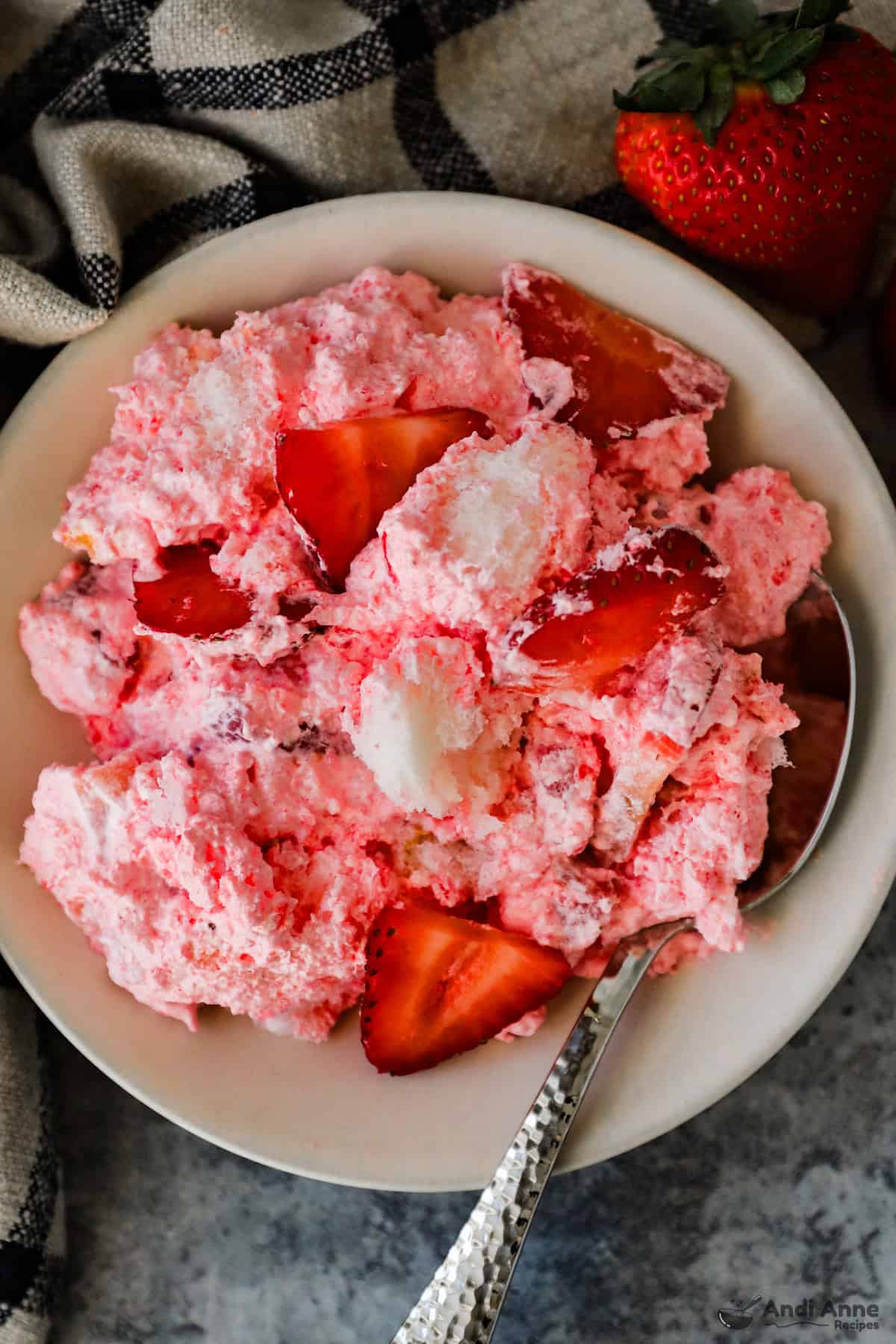 A bowl with a serving of fluffy angel food cake dessert with sliced strawberries.