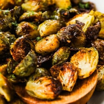 A serving dish with crispy roasted Brussels sprouts and a wooden spoon.