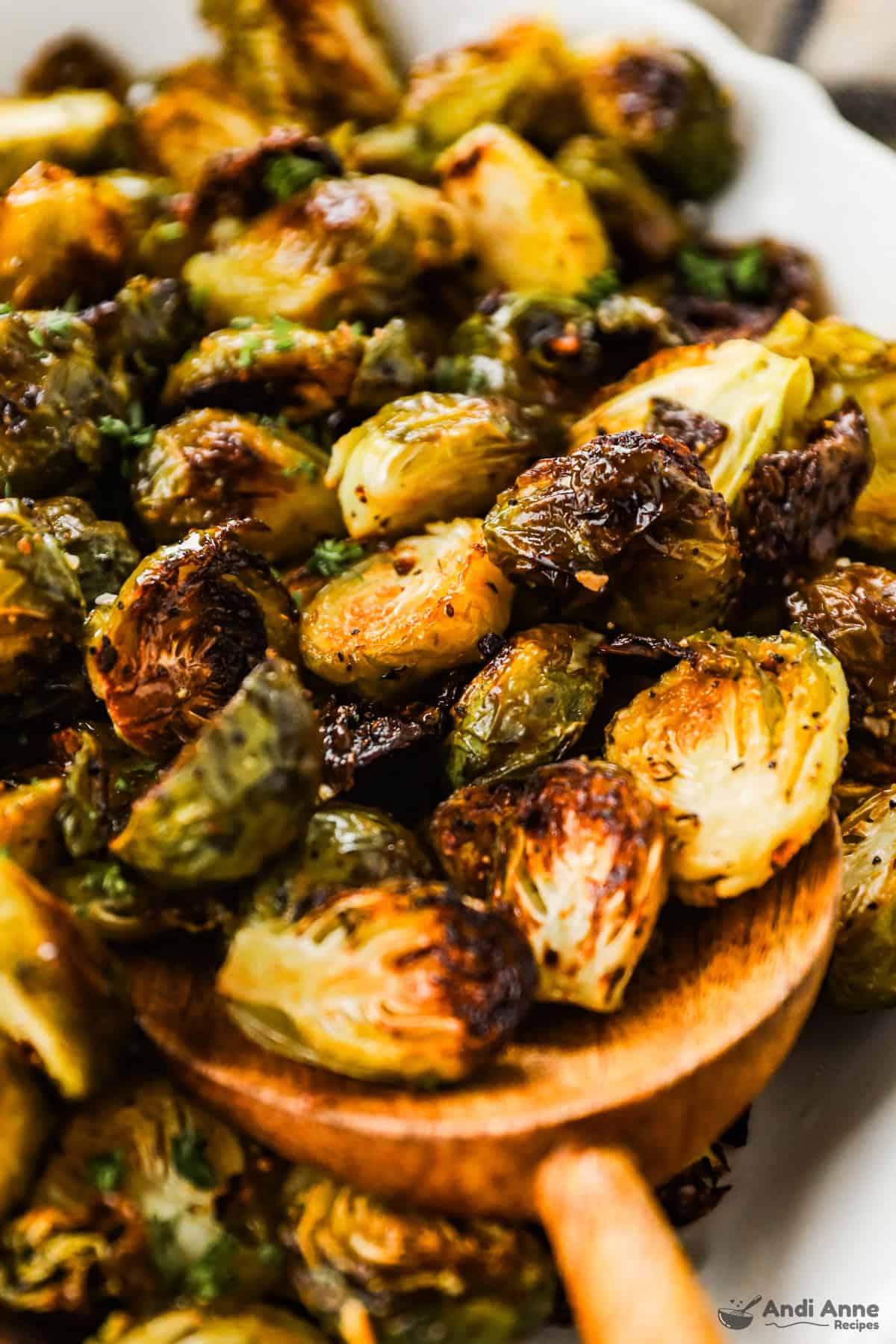 A serving dish with crispy roasted Brussels sprouts and a wooden spoon.