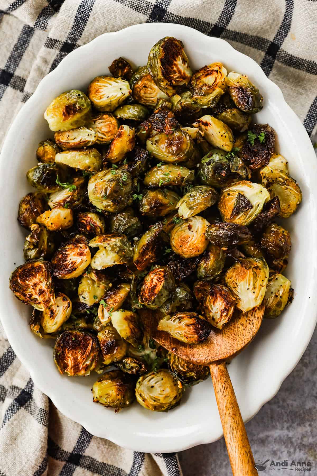 A serving dish of crispy roasted Brussels sprouts with a wooden spoon.
