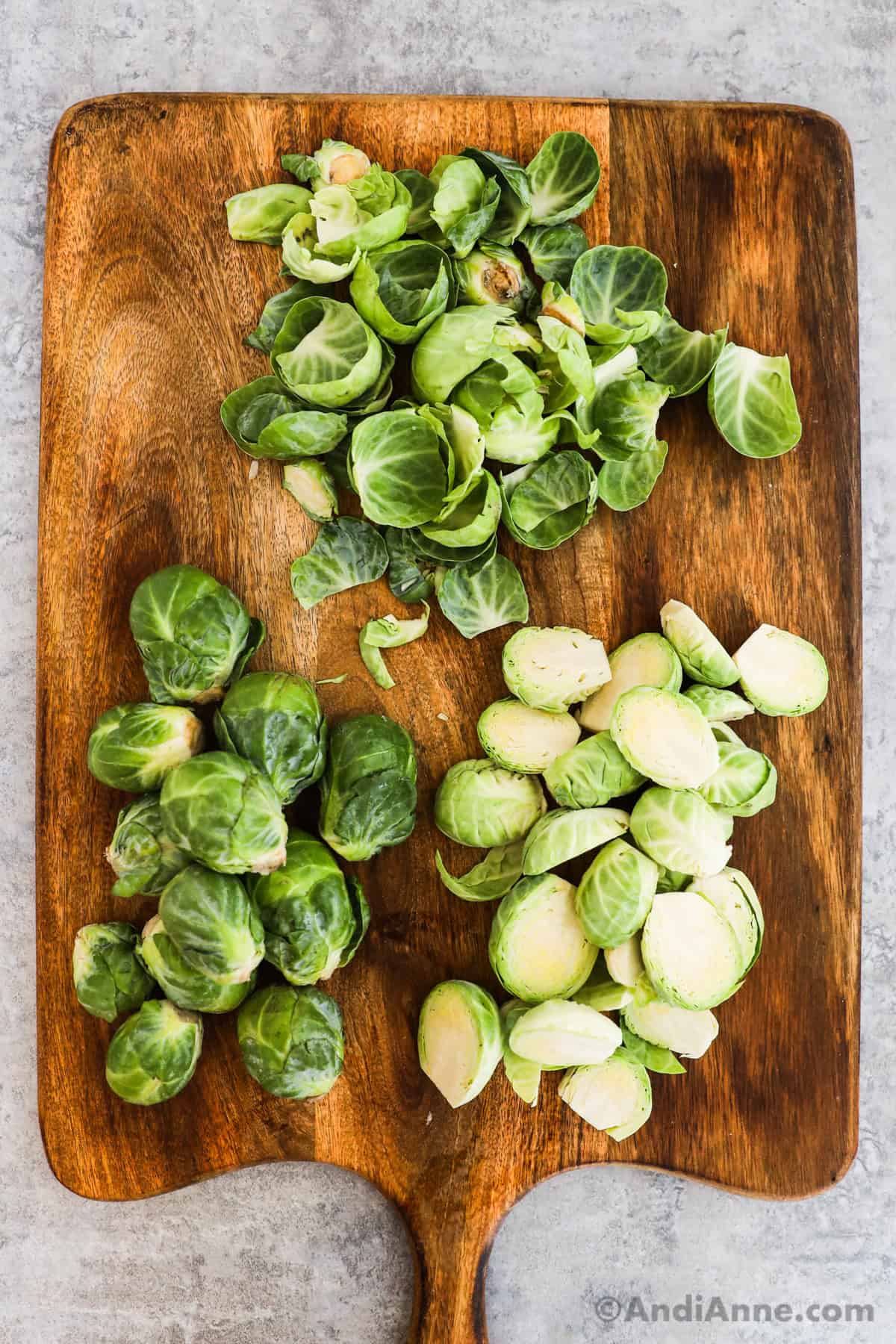 Brussels sprouts on a cutting board with the outer leaves removed and then halved.