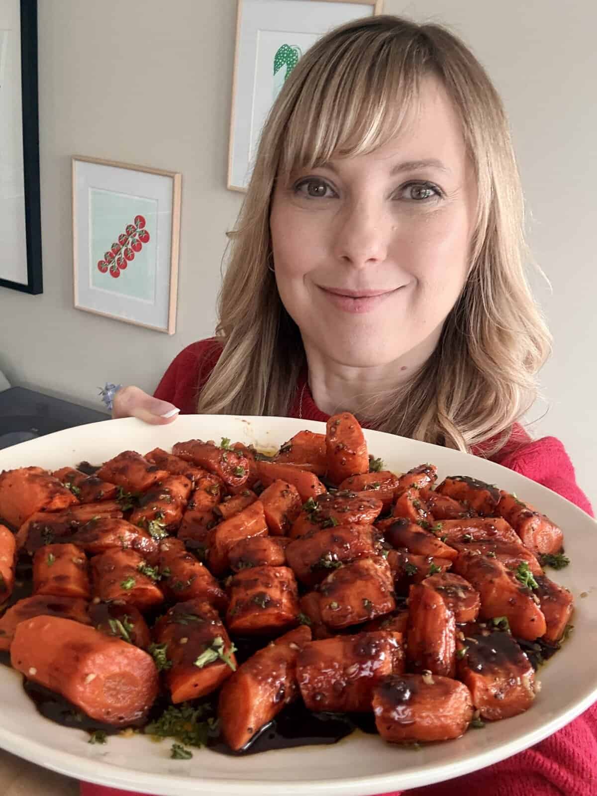 Andi is holding a serving dish of honey-balsamic roasted carrots.