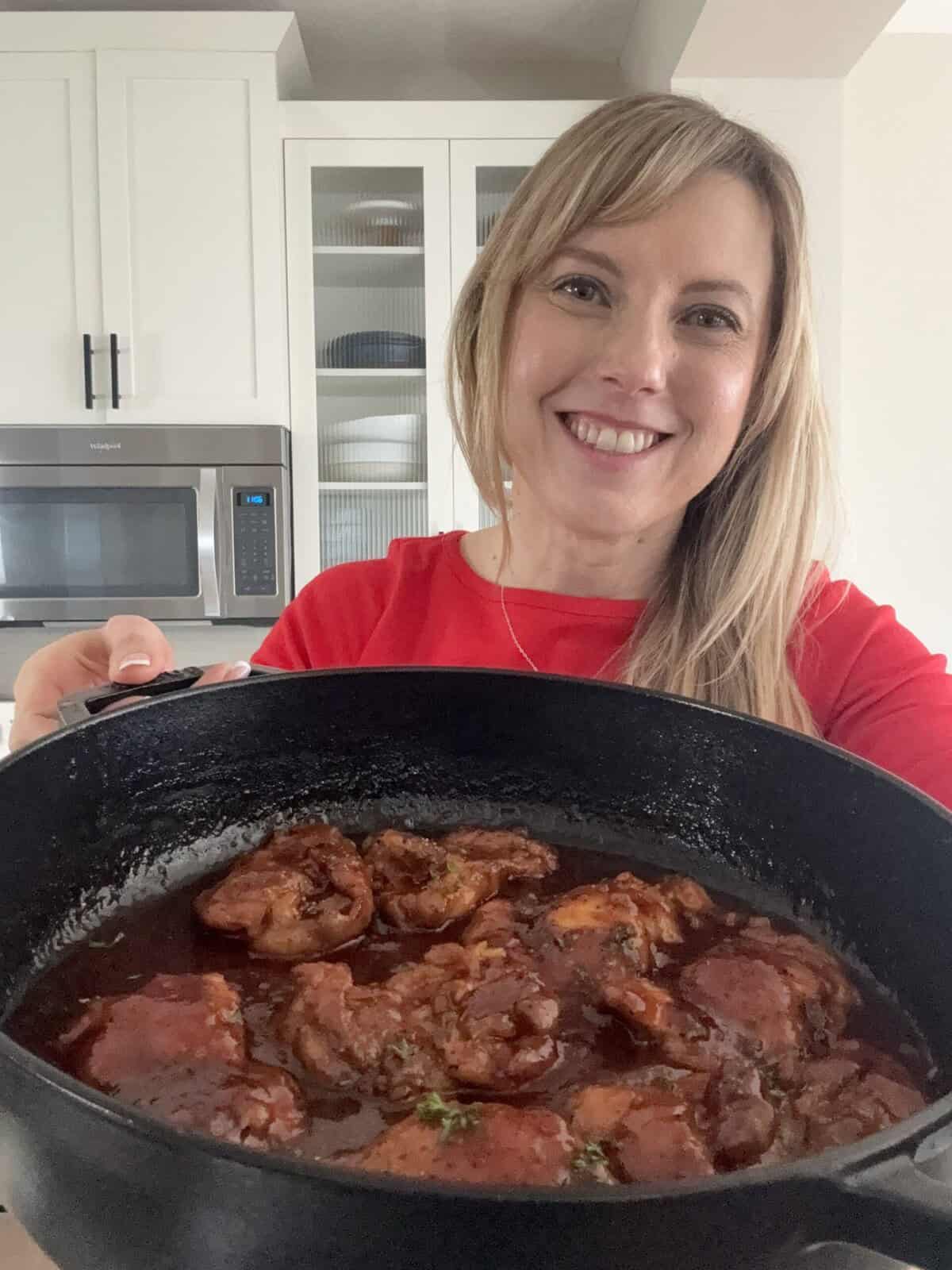 Andi is holding a skillet with boneless chicken thighs in a sweet and sour sauce.