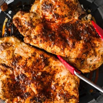 Tongs are lifting a cooked pork chop out of the air fryer.