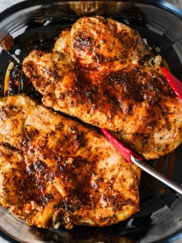 Tongs are lifting a cooked pork chop out of the air fryer.