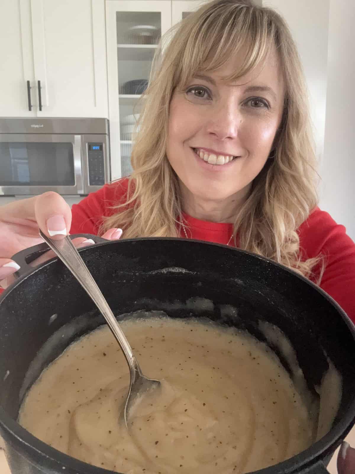 Andi is holding the pot of thick brown gravy, and a spoon is in the gravy.
