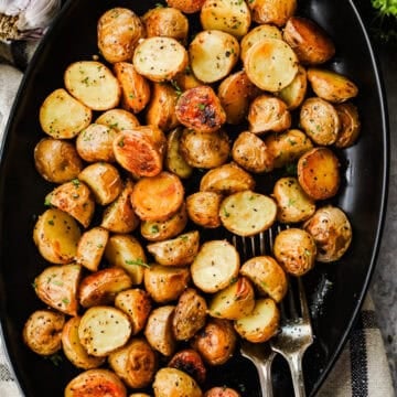 A serving dish with crispy roasted baby potatoes and two forks.