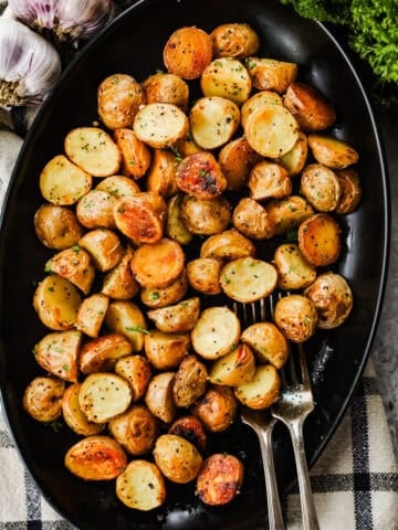 A serving dish with crispy roasted baby potatoes and two forks.