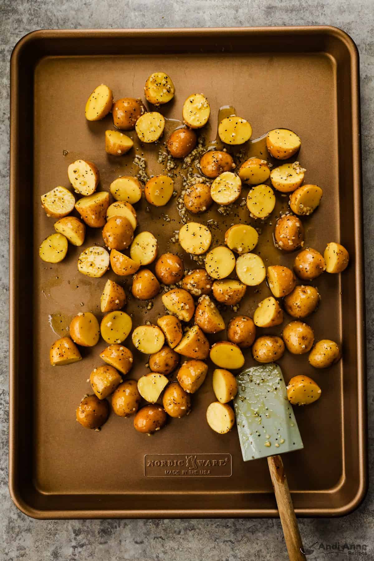 Baby potato halves on a large baking sheet with seasoning, garlic, and olive oil.