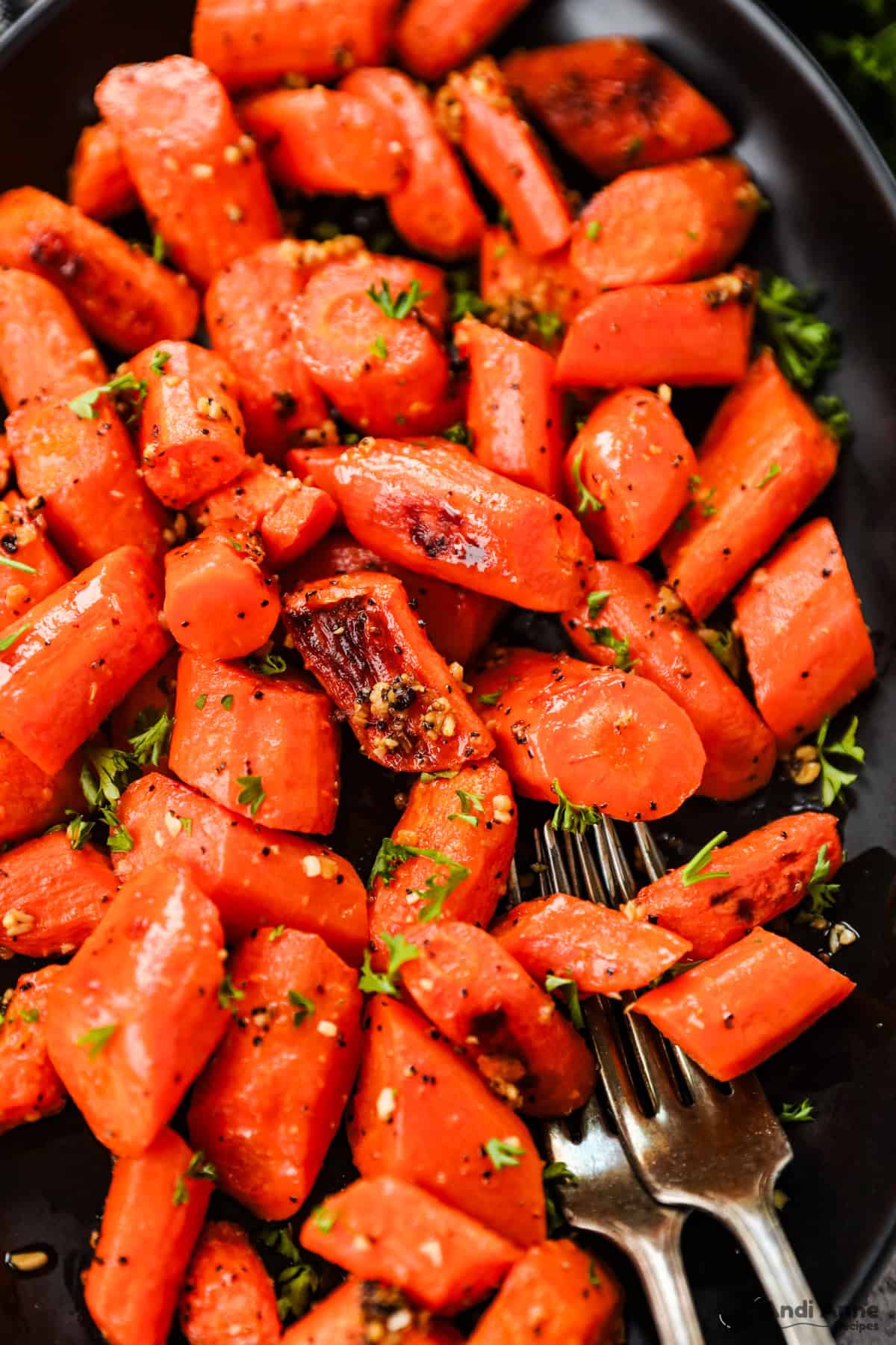 Roasted carrots with caramelized edges on a black serving dish.