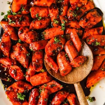 Roasted balsamic and honey roasted carrots on a serving dish with a wooden spoon.