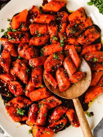 Roasted balsamic and honey roasted carrots on a serving dish with a wooden spoon.