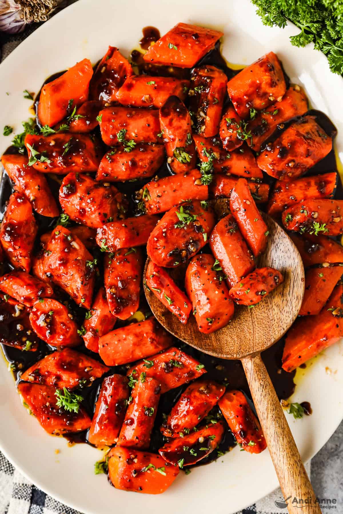 Roasted balsamic and honey roasted carrots on a serving dish with a wooden spoon.