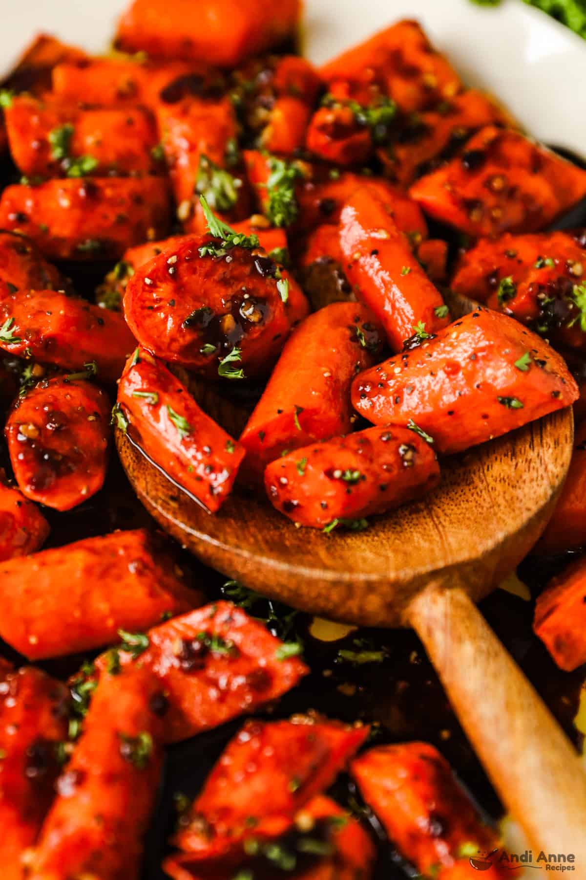 A wooden spoon with roasted carrots in a honey balsamic glaze.