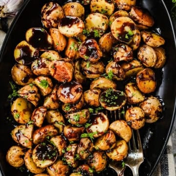 A large black serving dish with honey balsamic roasted baby potatoes and two forks.