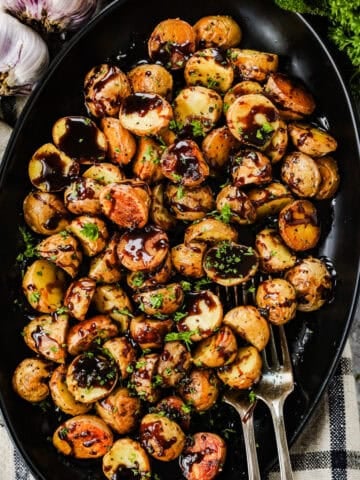 A large black serving dish with honey balsamic roasted baby potatoes and two forks.